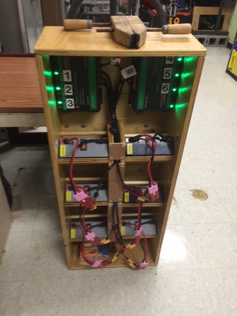 A wooden bookcase like cart for storing and charging batteries.